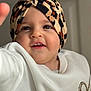 toddler, child, face, headwear, turban, leopard_print, white_sweater, heart_design, cute, smiling, portrait, indoor, baby, fashion, apparel, young_child, person, closeup, human, expression