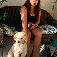 Bruno is registered to the contest to win money with this photo: black_shoes, casual_clothing, concrete_floor, cushion, dog, footwear, fur, headband, mug, outdoor, petting, plant, portrait, relaxation, seated, shadow, summer, sunlight, wicker_bench, woman