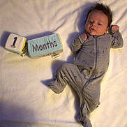 Heath is registered to the contest to win money with this photo: baby, bed, blanket, bodypart, clothing, face, finger, furniture, glove, hand, head, knitwear, longsleeve, newborn, pajamas, pants, person, photography, portrait, sweater