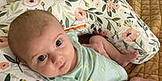 Gemma is registered to the contest to win money with this photo: baby, infant, nursing_pillow, onesie, bandage, blue_eyes, floral_pattern, bedroom, blanket, quilted, lying_down, curious_expression, person, child, skin, head, arm, foot, indoors, soft_lighting