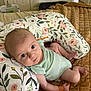 baby, infant, nursing_pillow, onesie, bandage, blue_eyes, floral_pattern, bedroom, blanket, quilted, lying_down, curious_expression, person, child, skin, head, arm, foot, indoors, soft_lighting