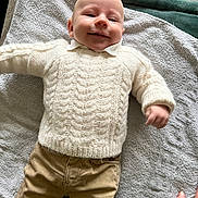 Gabriel a rejoint le concours — aidez-le/la à gagner de superbes lots ! baby, infant, smiling, sweater, knitwear, towel, blanket, lying_down, portrait, face, head, hand, khaki_pants, pants, clothing, cozy, indoor, wood_surface, texture, happy