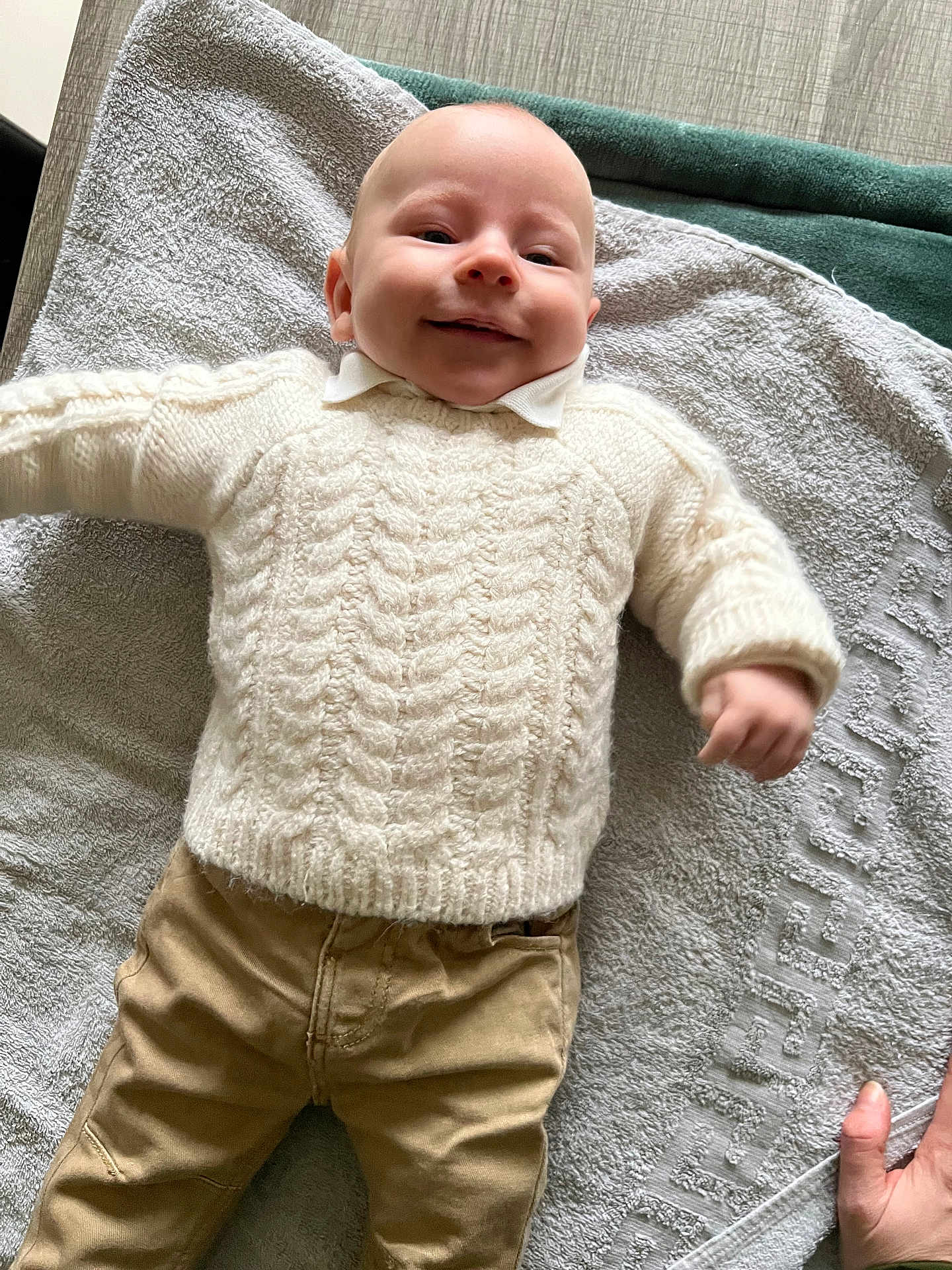 Gabriel a rejoint le concours — aidez-le/la à gagner de superbes lots ! baby, infant, smiling, sweater, knitwear, towel, blanket, lying_down, portrait, face, head, hand, khaki_pants, pants, clothing, cozy, indoor, wood_surface, texture, happy