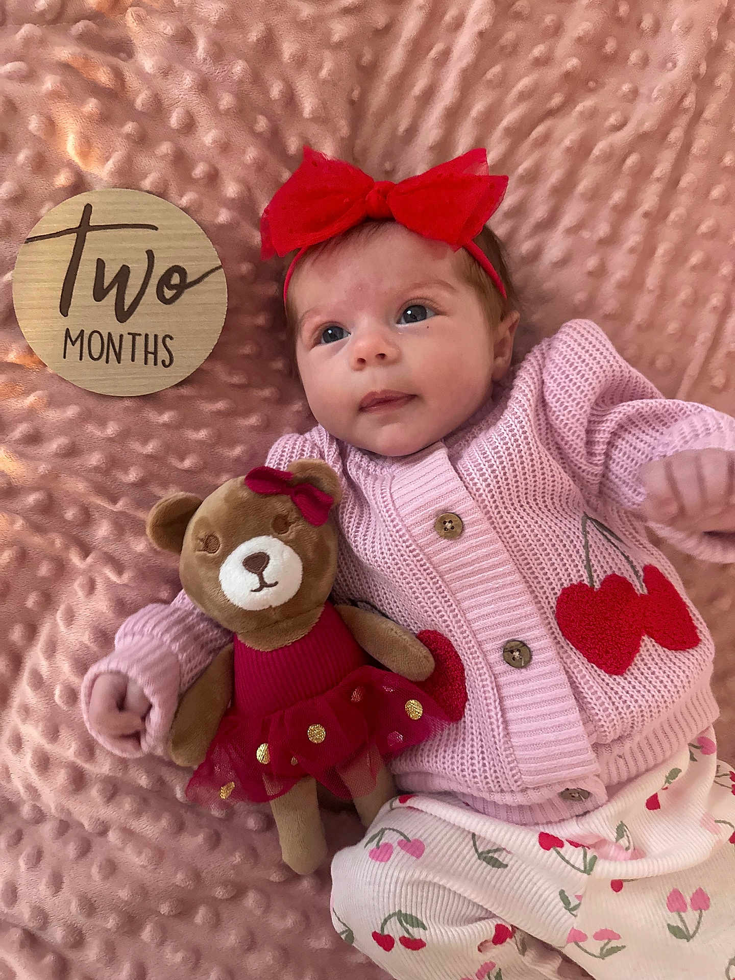Brystol is registered to the contest to win money with this photo: baby, infant, two_months, milestone_card, headband, red_bow, pink_blanket, knit_sweater, cherries_pattern, plush_bear, toy, button, lying_down, portrait, cute, wide_eyes, soft_texture, toddler_clothes, sleepwear, prop