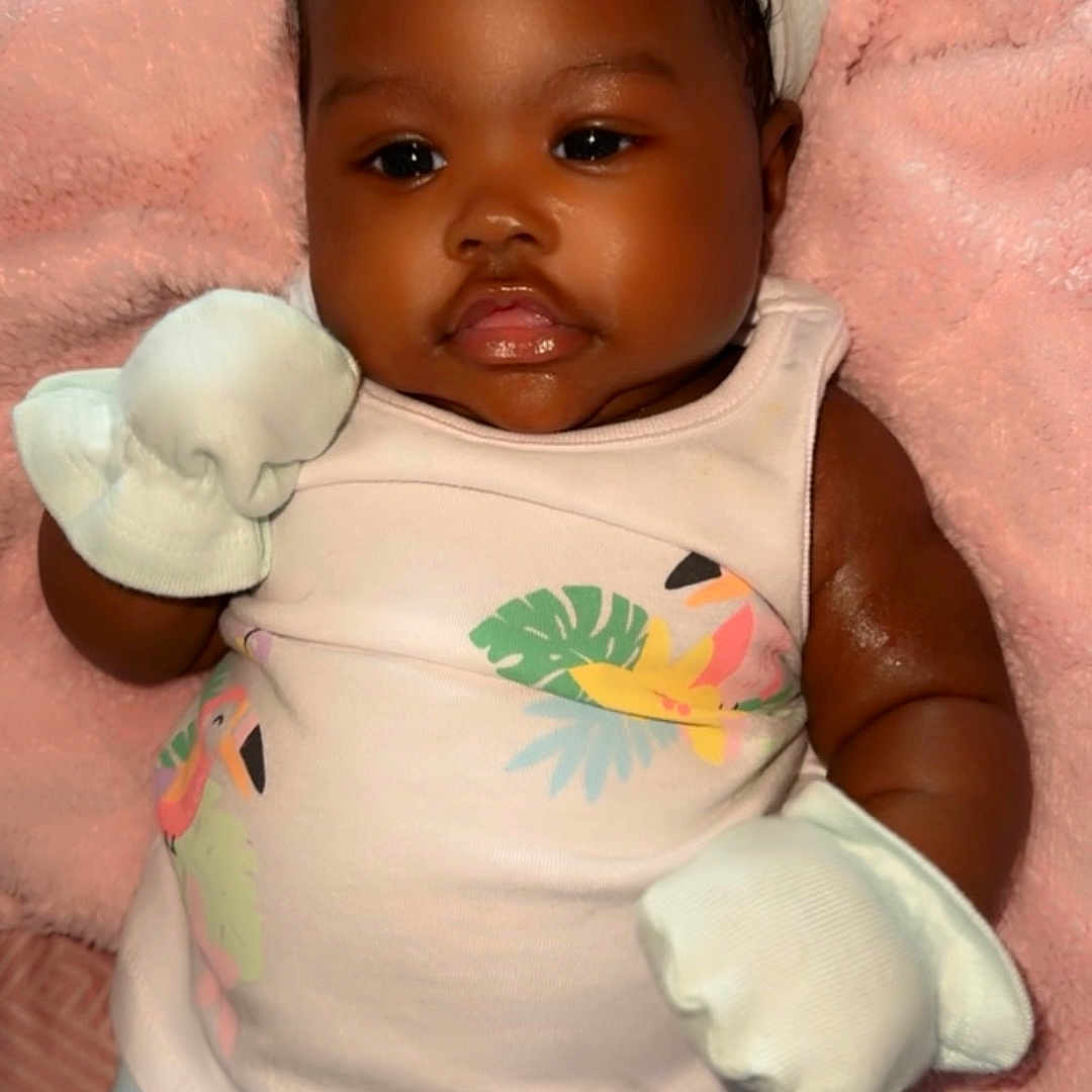 Aria is registered to the contest to win money with this photo: baby, bodypart, clothing, cushion, dress, face, glove, happy, hat, head, homedecor, mouth, newborn, person, photography, portrait, sitting, smile, t_shirt, toy