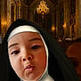 child, nun_costume, church, interior, chandelier, portrait, face, costume, religious, architecture, lighting, expression, playful, pout, person, indoor, gold, decor, curious, closeup