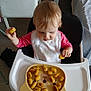 baby, bib, chair, child, clothing, curious, cute_plate, eating, floor, food, hair, high_chair, indoor, meal_time, person, plate, potato_bites, tableware, toddler, wooden_floor