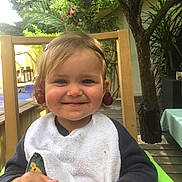 Lou a rejoint le concours — aidez-le/la à gagner de superbes lots ! toddler, child, smiling, cherry, bib, high_chair, outdoor, tree, wooden_chair, greenery, face, happy, person, nature, playful, fruit, cute, young_child, daylight, casual