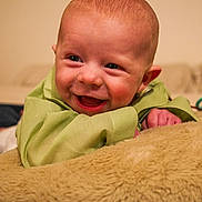 Atraeus is registered to the contest to win money with this photo: baby, infant, smiling, green_clothing, cushion, indoor, happy, face, head, child, person, lying_down, closeup, skin, cute, young, expression, comfort, soft, home