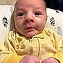 baby, infant, face, hands, yellow_clothing, onesie, cushion, feather_pattern, closeup, newborn, skin, expression, resting, indoor, portrait, child, cute, small_hands, eyes, young