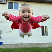 Melanie is registered to the contest to win money with this photo: baby, child, superhero, cape, flying, outdoor, grass, house, smiling, cute, portrait, playful, happy, infant, person, red_clothing, green_grass, daylight, window, background
