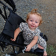 Journey joined the competition — help win amazing prizes! toddler, child, stroller, curly_hair, blue_eyes, leopard_print, outdoor, gravel, dirt, grass, footwear, hand, smile, person, seat, black, clothing, baby, cute, portrait