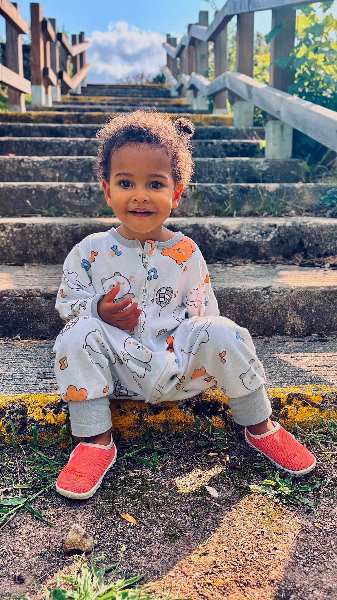 Aby participe au concours pour gagner de l'argent avec cette photo : child, toddler, stairs, outdoor, sunlight, onesie, patterned_clothing, smiling, curly_hair, red_shoes, grass, wooden_railing, nature, portrait, happy, casual, sitting, daylight, concrete, playful