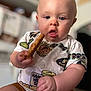 baby, child, cookie, food, messy_face, blue_eyes, shorts, tshirt, indoor, home, sitting, cute, chubby_cheeks, hand, mouth_open, blurred_background, person, infant, snack, curious