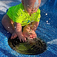 Creed Taylor joined the competition — help win amazing prizes! baby, child, water, splash, drain, blue_surface, neon_shirt, outdoor, sunlight, droplets, playing, curious, feet, hands, sitting, toddler, summer, fun, closeup, daytime