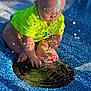 baby, child, water, splash, drain, blue_surface, neon_shirt, outdoor, sunlight, droplets, playing, curious, feet, hands, sitting, toddler, summer, fun, closeup, daytime