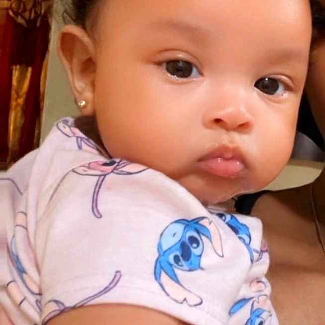 Brightyn joined the competition — help win amazing prizes! baby, child, infant, person, face, curly_hair, earrings, shirt, blue, cartoon_print, holding, arm, indoor, wall, mirror, heart_shape, decor, cute, expression, portrait