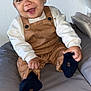 baby, child, smiling, overalls, sweater, sitting, indoors, cushion, couch, happy, person, face, footwear, sock, hand, head, skin, clothing, infant, portrait