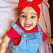 Nyra is registered to the contest to win money with this photo: baby, cherry_pattern, child, closeup, clothing, cute, denim_overalls, face, happy, headwear, hello_kitty, human, indoor, infant, joyful, pink_blanket, portrait, red_headband, smiling, toddler