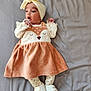apparel, baby, bow, child, curious, cute, dress, expression, footwear, fox_design, gray_sheet, headband, indoors, infant, lying_down, newborn, patterned_tights, small_hands, soft_fabric, white_shoes