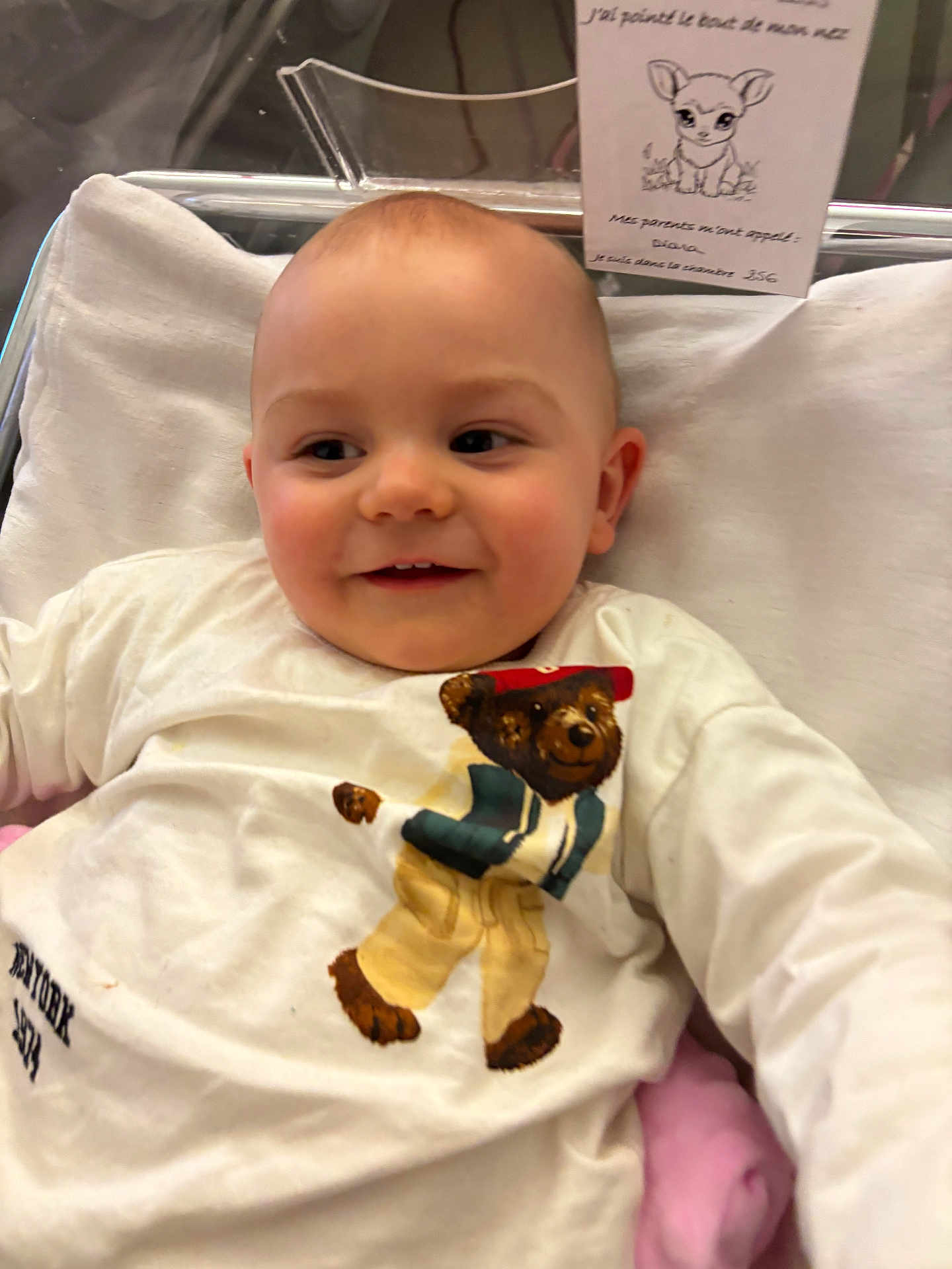 Hayden a rejoint le concours — aidez-le/la à gagner de superbes lots ! baby, smiling, crib, white_shirt, bear_illustration, blanket, infant, child, portrait, cute, happy, indoors, person, clothing, face, head, soft, comfortable, lying_down, young_child