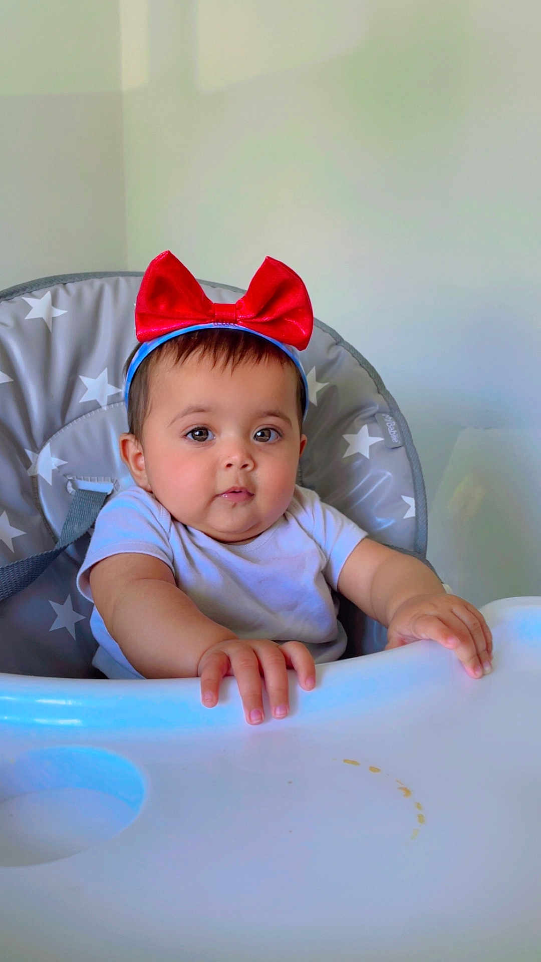Ayzal is registered to the contest to win money with this photo: baby, high_chair, red_bow, headband, infant, child, face, hands, expression, clothing, indoor, furniture, star_pattern, person, portrait, cute, baby_girl, sitting, table, feeding_chair