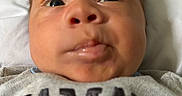 Bolivar is registered to the contest to win money with this photo: baby, infant, closeup, face, expression, clothing, shirt, text, portrait, curious, young_child, skin, head, eyes, mouth, nose, indoors, blurred_background, person, human