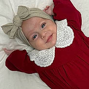 Fiadh joined the competition — help win amazing prizes! baby, infant, smile, headwrap, bow, red_dress, white_collar, lying_down, blanket, face, child, cute, portrait, happy, blue_eyes, skin, hands, clothing, indoors, soft_lighting