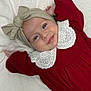 baby, infant, smile, headwrap, bow, red_dress, white_collar, lying_down, blanket, face, child, cute, portrait, happy, blue_eyes, skin, hands, clothing, indoors, soft_lighting