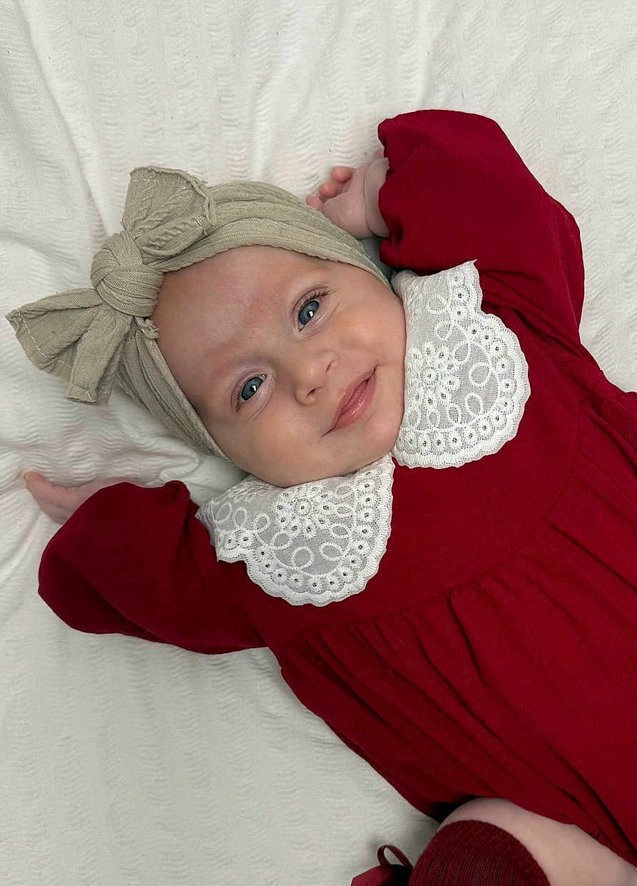Fiadh joined the competition — help win amazing prizes! baby, infant, smile, headwrap, bow, red_dress, white_collar, lying_down, blanket, face, child, cute, portrait, happy, blue_eyes, skin, hands, clothing, indoors, soft_lighting
