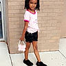 Skylah is registered to the contest to win money with this photo: child, girl, posing, brick_wall, sidewalk, pink_shirt, black_shorts, black_shoes, butterfly_purse, hair_bows, outdoor, casual, fashion, young, standing, confident, accessory, person, daylight, urban