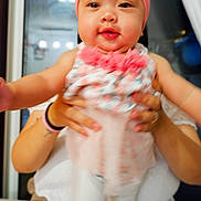 Erzabelle is registered to the contest to win money with this photo: baby, child, pink_bow, headband, floral_top, white_pants, hands, adult, indoor, curious, blurry, portrait, cute, smiling, infant, person, holding, face, closeup, home