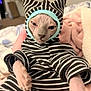 bed, blanket, cat, costume, cozy, cute, ears, expression, face, hairless_cat, human_hand, indoor, paws, pet, pink_blanket, portrait, sphynx_cat, striped_onesie, stripes, wrinkled_skin