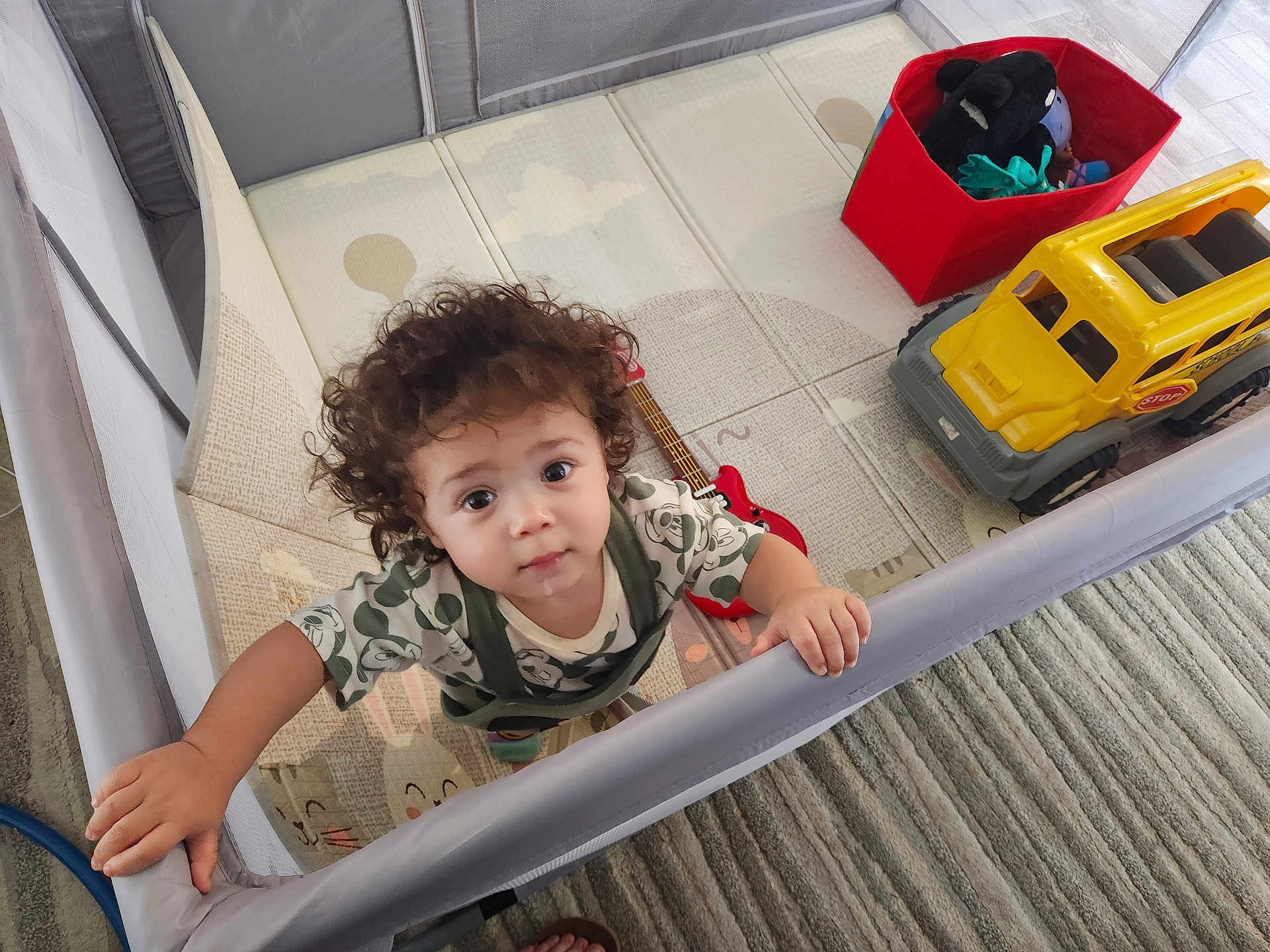 Jaxon joined the competition — help win amazing prizes! toddler, child, curly_hair, playpen, toy_truck, toy_guitar, floor_mat, indoor, carpet, drool, cute, looking_up, hand_grip, expression, soft_lighting, home, play_area, baby_clothes, person, young_child
