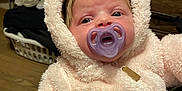Milani is registered to the contest to win money with this photo: baby, pacifier, onesie, fluffy, bear_ears, infant, clothing, face, indoor, cute, portrait, child, young, warm, soft_texture, person, looking, expression, hood, cozy