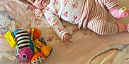 Lily is registered to the contest to win money with this photo: baby, infant, blanket, plush_toy, clothing, striped_pants, floral_sweater, pink, soft_texture, elephant_design, lying_down, indoor, child, cute, toy, pastel_colors, smiling, face, small_hands, comfort