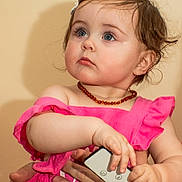 Ava is registered to the contest to win money with this photo: toddler, child, baby, pink_dress, blue_eyes, remote_control, hands, adult_hands, portrait, indoor, curious, looking_away, jewelry, necklace, short_hair, skin, human, person, cute, innocent