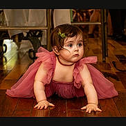 Ava is registered to the contest to win money with this photo: baby, child, crawling, curious, cute, expression, eyes, flooring, furniture, hair, hair_clip, hands, indoor, necklace, person, pink_dress, portrait, skin, wooden_floor, young_child
