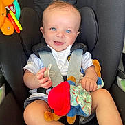 Archie is registered to the contest to win money with this photo: baby, infant, car_seat, smiling, blue_eyes, pacifier, plush_toy, red_hat, white_shirt, shorts, socks, child, happy, cute, seatbelt, toy, indoor, portrait, person, young