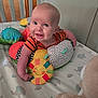 baby, child, smiling, crib, pillow, plush_toy, colorful, polka_dots, elephant_pattern, bedding, infant, happy, cute, indoors, person, toy, orange_clothing, head, face, arm