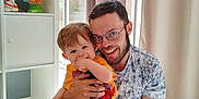 Nino participe au concours pour gagner de l'argent avec cette photo : child, adult, smile, happy, indoor, window, curtains, toy, sitting, floor, casual_clothing, glasses, light, family, playful, person, young_man, toddler, home, interaction