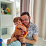 child, adult, smile, happy, indoor, window, curtains, toy, sitting, floor, casual_clothing, glasses, light, family, playful, person, young_man, toddler, home, interaction