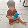 Nino participe au concours pour gagner de l'argent avec cette photo : toddler, child, toy, phone, indoor, floor, tile, brown_clothing, sitting, curious, young_child, play, hands, feet, short_hair, home, light, minimal, casual, interior