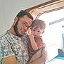 man, child, toddler, glasses, beard, indoor, holding, curious, fingers, brown_hair, short_sleeve, white_wall, door_frame, radiator, tile_floor, smile, person, home, light, casual