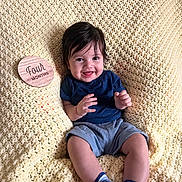 Josiah joined the competition — help win amazing prizes! baby, infant, smiling, knitted_blanket, blue_socks, navy_shirt, gray_shorts, wooden_plaque, four_months, milestone, happy, cute, sitting, portrait, indoors, child, young, soft_texture, cozy, candid