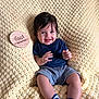 baby, infant, smiling, knitted_blanket, blue_socks, navy_shirt, gray_shorts, wooden_plaque, four_months, milestone, happy, cute, sitting, portrait, indoors, child, young, soft_texture, cozy, candid