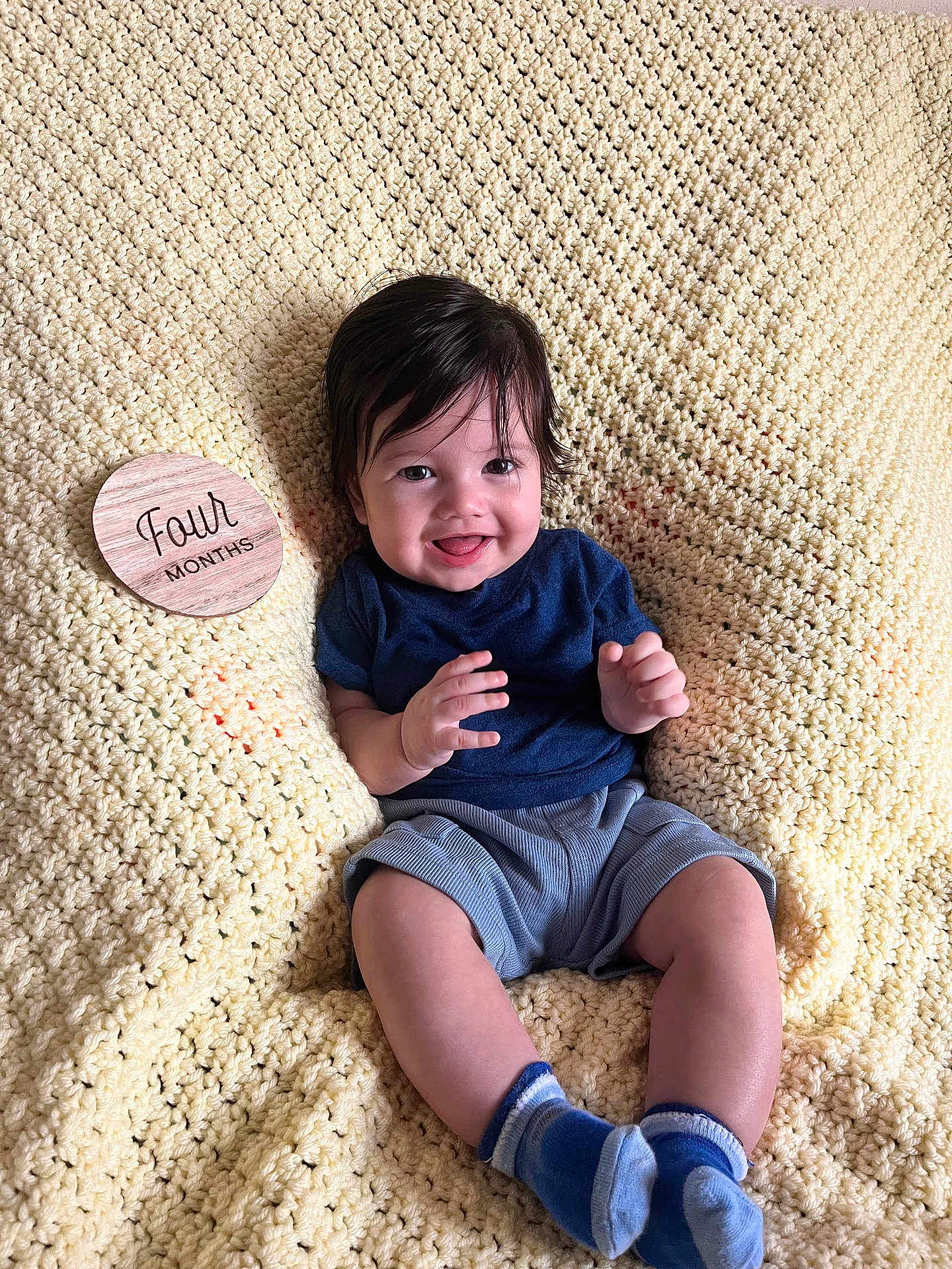 Josiah joined the competition — help win amazing prizes! baby, infant, smiling, knitted_blanket, blue_socks, navy_shirt, gray_shorts, wooden_plaque, four_months, milestone, happy, cute, sitting, portrait, indoors, child, young, soft_texture, cozy, candid