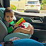 child, toddler, car_seat, toy, barefoot, car_interior, window, seatbelt, person, green_clothing, foot, hand, vehicle, parking, outside, daylight, face, hair, seat, plastic_toy