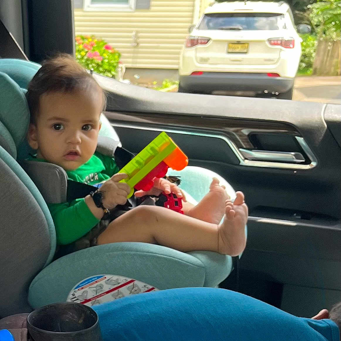 Ayasha joined the competition — help win amazing prizes! barefoot, car_interior, car_seat, child, daylight, face, foot, green_clothing, hair, hand, outside, parking, person, plastic_toy, seat, seatbelt, toddler, toy, vehicle, window