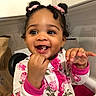 baby, chair, child, close_up, curly_hair, family_photo, floral_outfit, girl, hair_bows, happy, high_chair, indoor, kitchen, pink_clothing, portrait, reaching, sitting, smiling, teeth, toddler